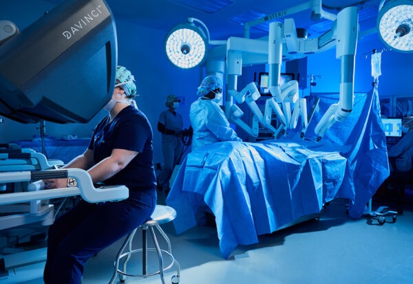 A medical professional operates a Da Vinci surgical robot while a team assists with a patient